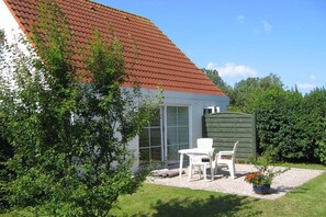 A house with a sloped red roof, a white exterior, and a small patio with white chairs and a table. - Holiday home with 1 bedroom (Wyk auf Föhr)