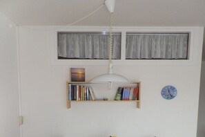 Une pièce avec un ventilateur de plafond, une étagère remplie de livres, une horloge et une fenêtre avec des rideaux.