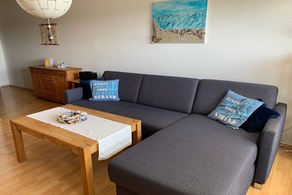 Uma sala de estar moderna com um sofá cinzento, mesa de centro de madeira e almofadas decorativas.