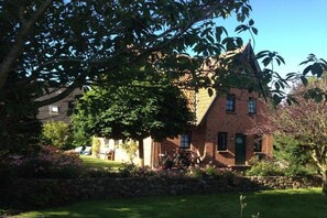 A brick building with a tower, surrounded by a stone wall and greenery. - Holiday home in Oldsum with swimming pool (Oldsum)