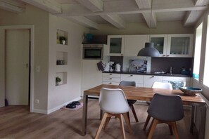 A compact kitchen with white cabinets, a wooden dining table, and a large window. - Holiday home in Oldsum with swimming pool (Oldsum)