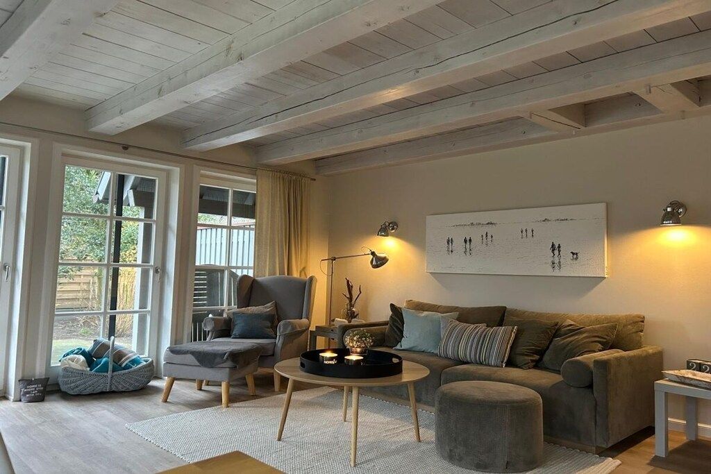 A cozy living room with a sofa, armchair, and coffee table, featuring a large window and a wall-mounted artwork.
