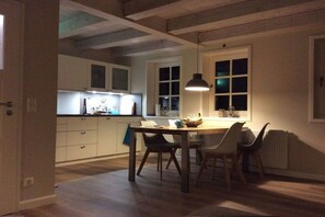 A kitchen with white cabinets, a dining table with chairs, and a hanging pendant light. - Holiday home in Oldsum with swimming pool (Oldsum)