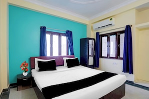 A hotel room with a bed, a nightstand, a vase with flowers, a wardrobe, and an air conditioning unit. - Hotel O Chitrakut Nagar Royal Brothers (Danapur)
