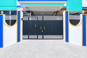 Uma entrada com portão, caminho de concreto e um edifício com paredes azuis e brancas.