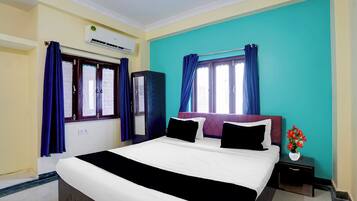 Quarto de hotel com cama, mesa de cabeceira, um vaso com flores e janela com cortinas.
