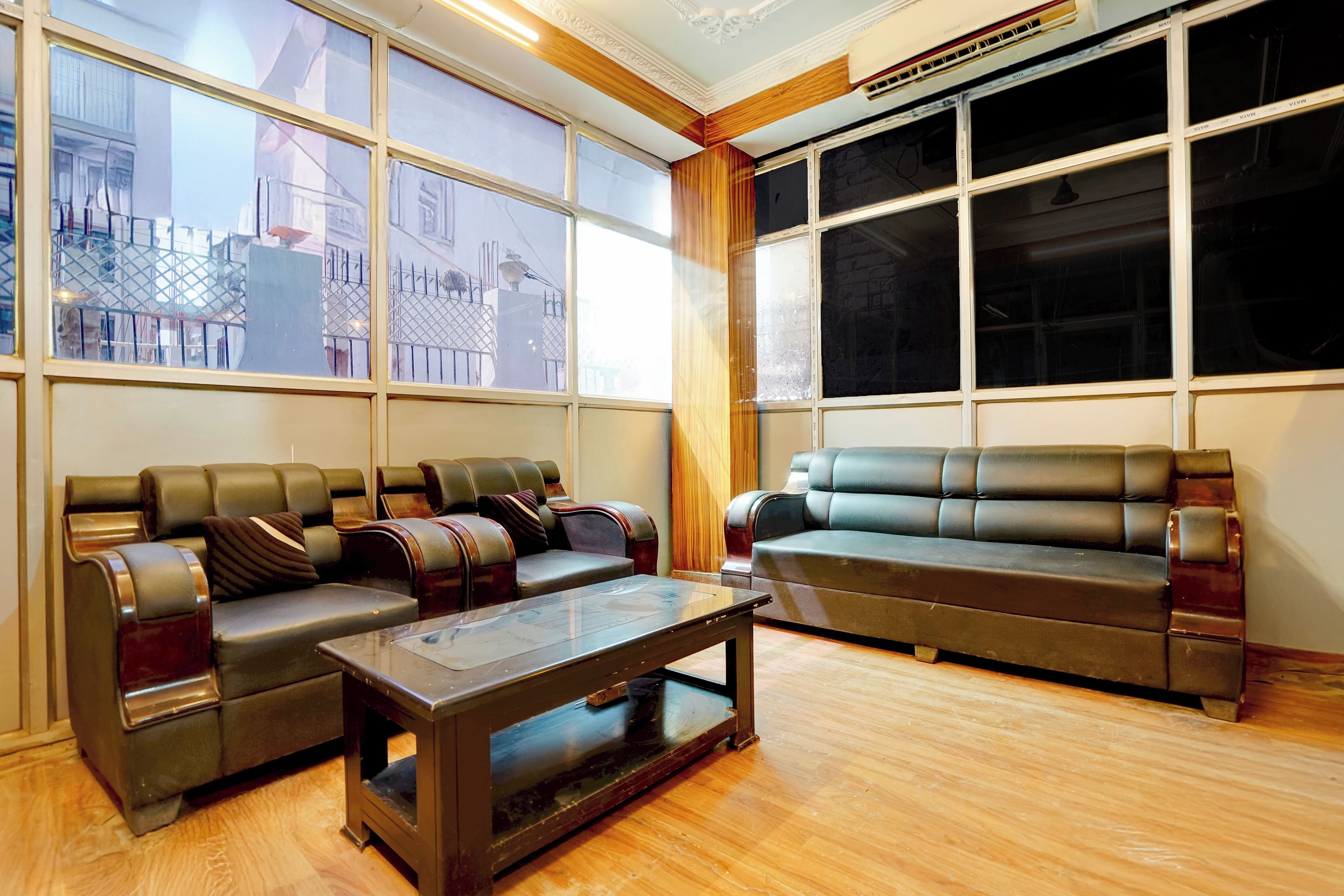 A room with a seating area featuring leather sofas and armchairs, a glass coffee table, and large windows offering views of the outside.