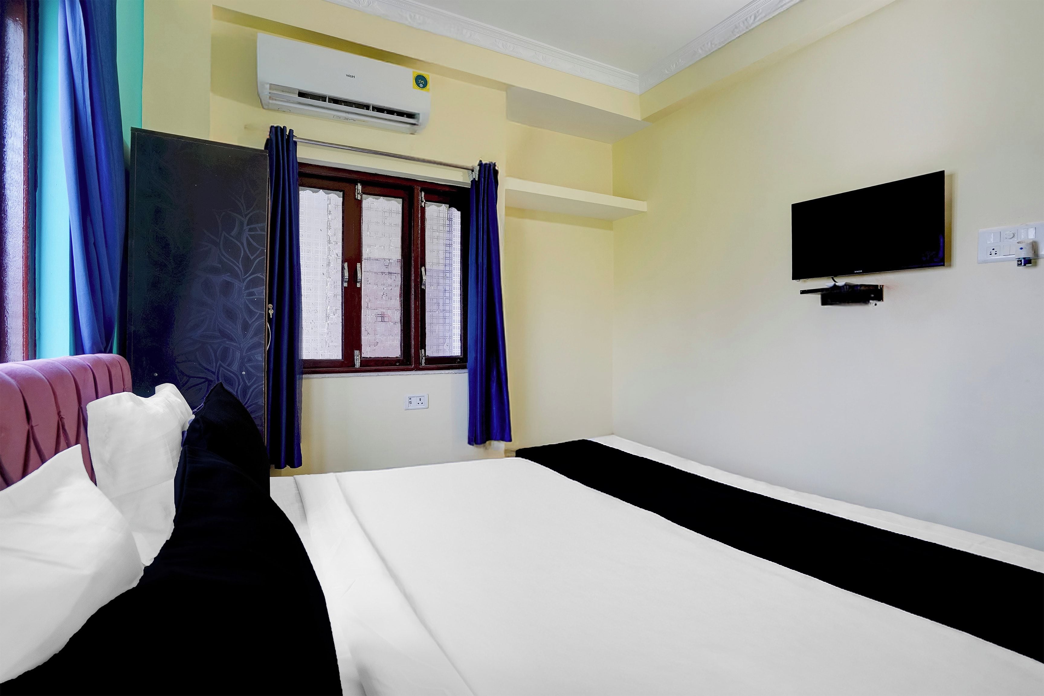 Habitación de hotel con cama, televisor, aire acondicionado y ventana con cortinas.