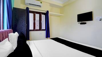 Habitación de hotel con cama, televisor, aire acondicionado y ventana con cortinas.
