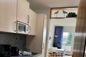 A compact kitchen with a microwave, coffee maker, and a dining area with a table and chairs. - Berliner Ring - Apt. 27 (Wyk auf Föhr)