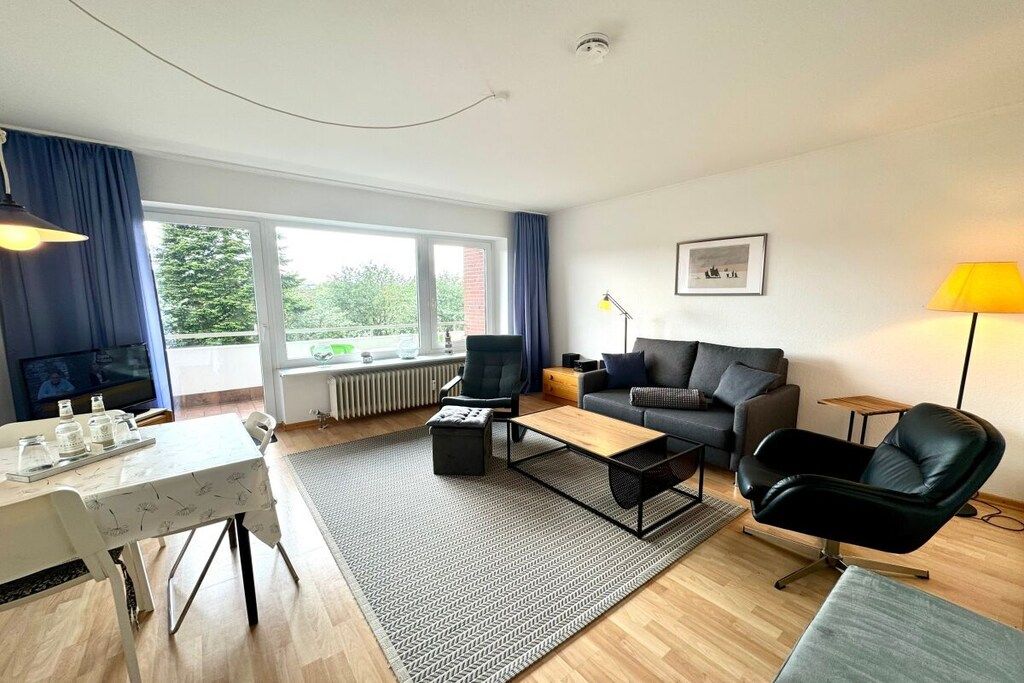 A modern living room with a sofa, armchairs, a coffee table, and a dining area with a table and chairs.