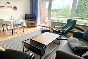 A living room with a sofa, a coffee table, a TV, and a dining area with chairs and a table. - Berliner Ring - Apt. 27 (Wyk auf Föhr)
