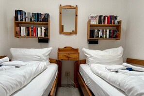 A room with two beds, a small wooden nightstand, and two bookshelves filled with books. - Berliner Ring - Apt. 27 (Wyk auf Föhr)