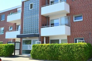 A multi-story residential building with balconies, a glass facade, and a well-maintained hedge in front. - Berliner Ring - Apt. 27 (Wyk auf Föhr)