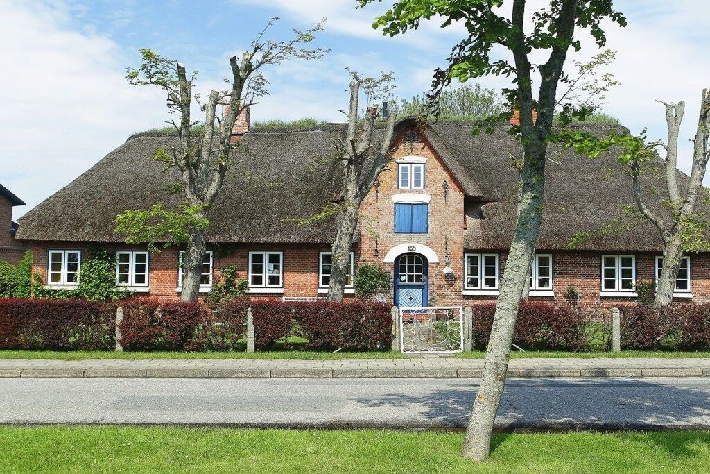 A traditional brick house with a thatched roof, a central chimney, and a blue door.