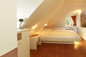 Ein Schlafzimmer mit schrägverdeckter Decke, einem Bett, einem Nachttisch und einem Fenster mit Vorhängen.
