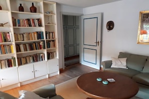 Ein Wohnzimmer mit rundem Couchtisch, Bücherregal, einer Couch und einer Tür zu einem anderen Raum.