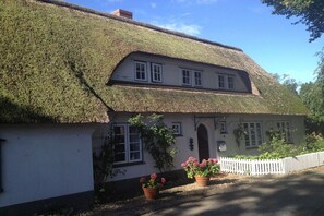 A traditional house with a thatched roof, white walls, and a white picket fence. - Garden apartment in the Muschel house (Nieblum)