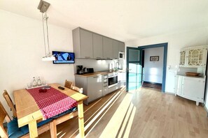 A compact living space with a dining table, kitchen area, and a television mounted on the wall. - Garden apartment in the Muschel house (Nieblum)