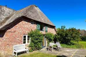 A thatched-roof house with a brick exterior, a bench, and a table outside. - Holiday home in Oldsum with swimming pool (Oldsum)