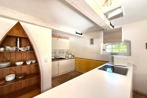 A kitchen with white cabinets, a wooden shelf with dishes, a window, and a built-in stove. - Holiday home in Oldsum with swimming pool (Oldsum)