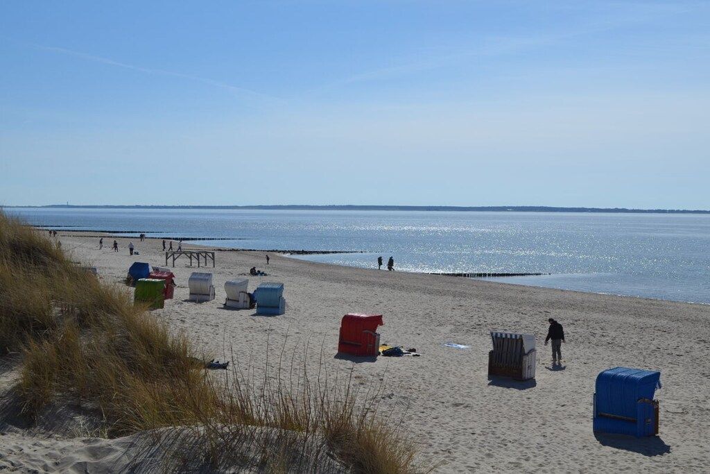 A beach with sand, a body of water, and a pier in the distance.