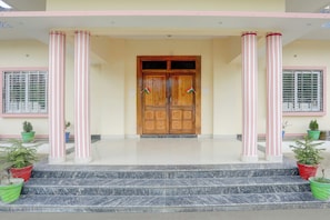 A building entrance with a wooden double door, two potted plants, and a tiled floor. - Hotel O IIT Varanasi Shree Gopal Upwan  (Varanasi)