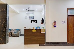 Zona d'entrada d'hotel amb taulell de recepció, rellotge, ventilador de sostre i extintor.