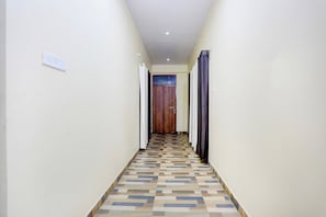 Un passadís amb un paviment estampat, una porta de fusta al final i un interruptor de llum a la paret.