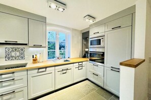 A modern kitchen with white cabinets, a built-in oven, and a window providing natural light. - Holiday apartment with 2 bedrooms (Oldsum auf Föhr)