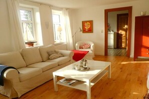 A living room with a sofa, a coffee table, a chair, and a painting on the wall. - Holiday apartment with 2 bedrooms (Oldsum auf Föhr)