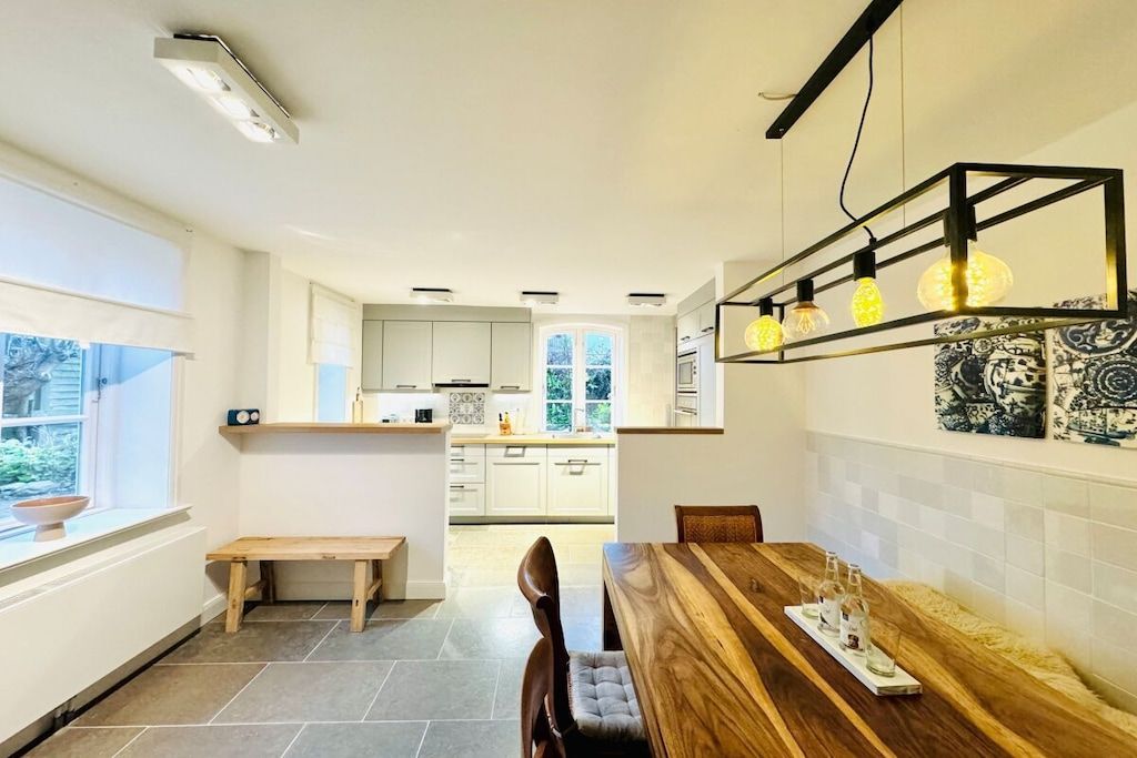 A modern kitchen with white cabinets, a wooden dining table, and pendant lighting.