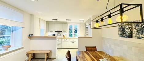 A modern kitchen with white cabinets, a wooden dining table, and pendant lighting.