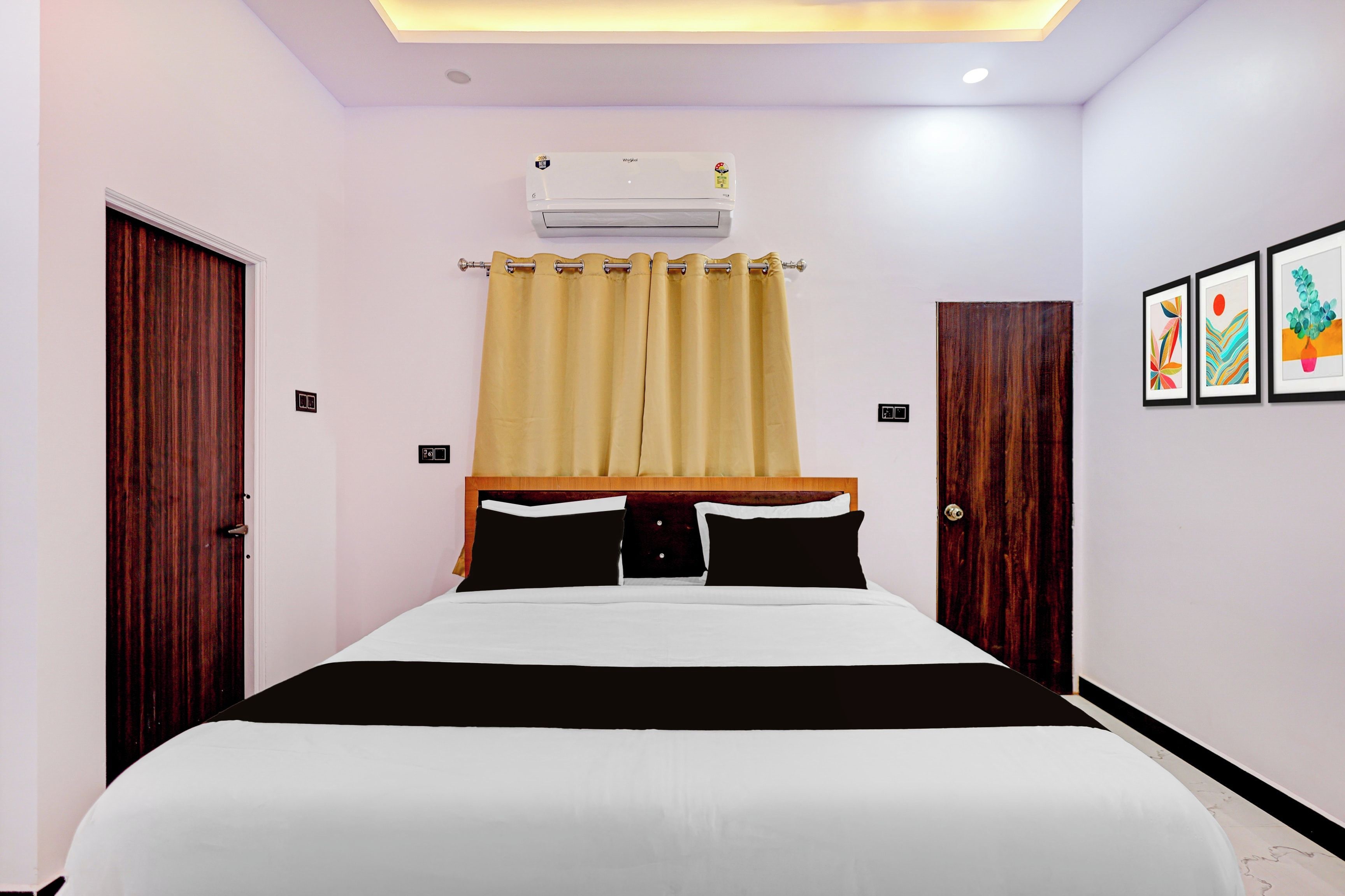 A hotel room with a bed, an air conditioning unit, a curtain, and artwork on the wall.