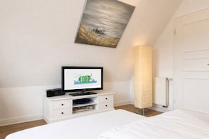 Ein Hotelzimmer mit einem Bett, einem Fernseher auf einer weißen Kommode, einem Gemälde an der Wand und einer hohen Lampe.