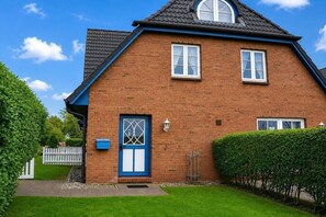 Ein zweistöckiges Backsteinhhaus mit blauer Tür, zwei Fenstern und einer kleinen Veranda.