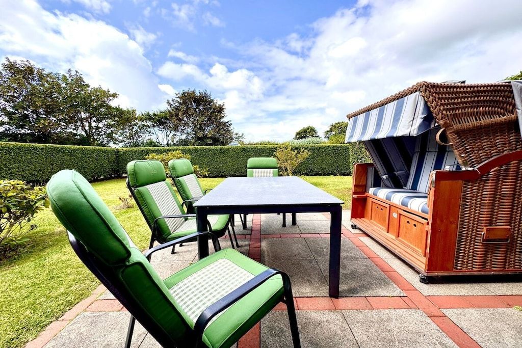 An outdoor patio area with a table and chairs, a wicker sofa, and a well-maintained hedge.