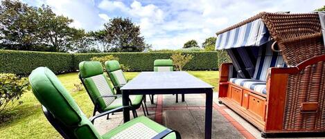 An outdoor patio area with a table and chairs, a wicker sofa, and a well-maintained hedge.