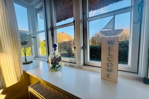 A window with a welcome sign, a bottle with flowers, and a lamp on a windowsill. - Rectory Courtyard - House Section 4 (Wrixum)