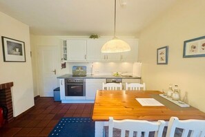 A compact kitchen with white cabinets, a wooden dining table, and a hanging light fixture. - Rectory Courtyard - House Section 4 (Wrixum)