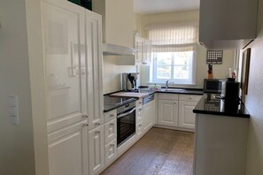 A kitchen with white cabinetry, a built-in oven, a microwave, and a window with curtains. - 5 in the Deichhof house (Dunsum)