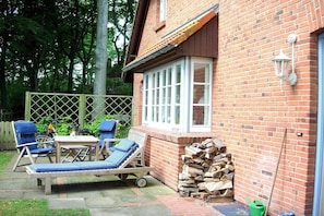 A brick house with a patio area, a wooden table, two lounge chairs, and a window. - Holiday home at the spa park 1a (Wyk auf Föhr)