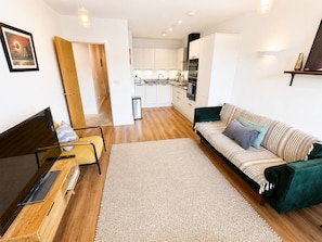 Een moderne woonkamer met een bank, televisie en een eethoek, met een keuken op de achtergrond.