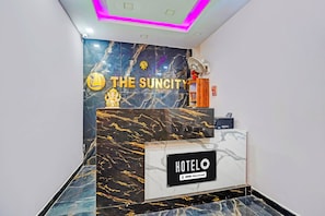 A reception desk with a marble wall, a sign reading 'THE SUNCITY HOTELO', and a fan on the wall. - Hotel O Patliputra Golmber Patna Suncity (Patna)