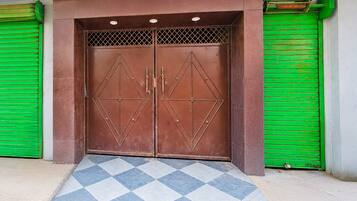 Una puerta doble con diseños geométricos, flanqueada por contraventanas verdes y un acceso con baldosas estampadas.