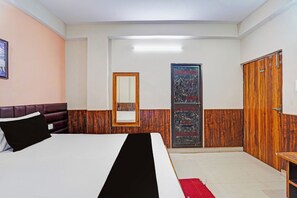 A hotel room with a bed, a wooden wardrobe, a mirror, and a door with a decorative panel. - Hotel O Patliputra Golmber Patna Suncity (Patna)