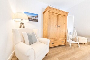 Een kamer met een witte bank, een houten garderobe, een witte stoel en een witte vloerlamp.