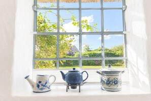 Une fenêtre donnant sur un jardin et une maison, et deux théières posées sur le rebord de la fenêtre.