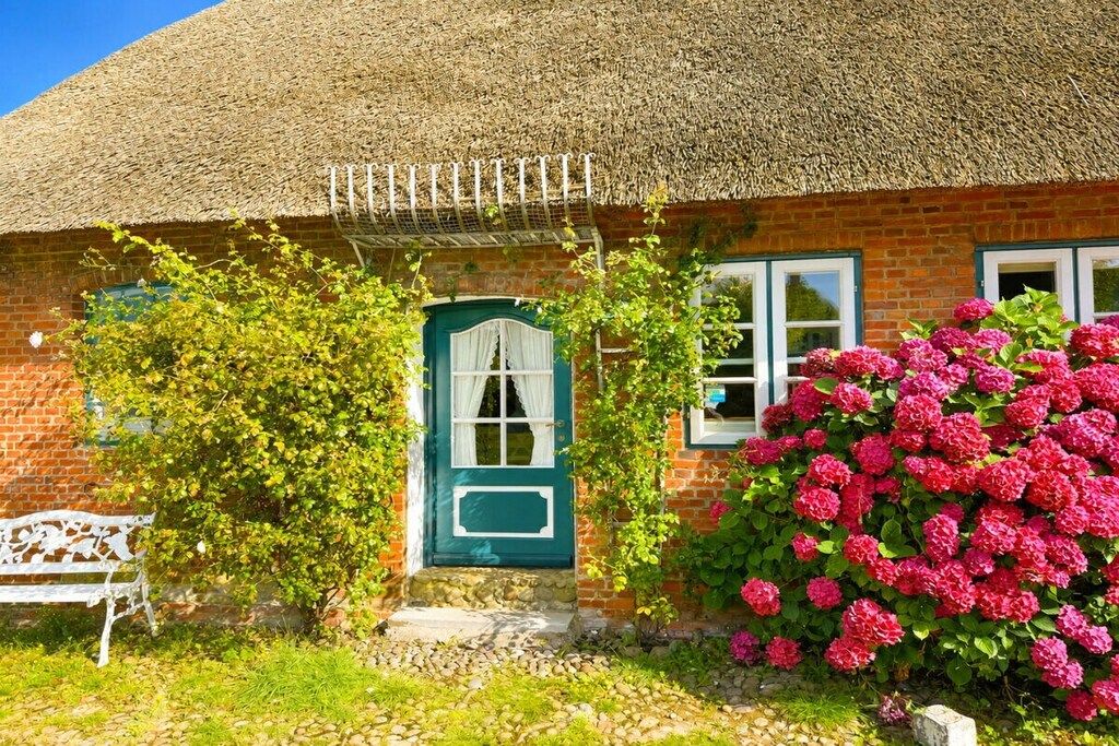Una casa de ladrillo con techo de paja, una puerta verde y un banco.