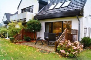 Ein Wohnhaus mit überdachter Terrasse, Gartenmöbeln im Freien und einem Garten mit Hortensien.
